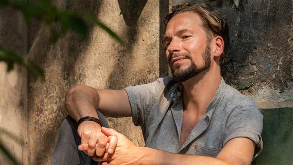 Sänger Felix Räuber lehnt im Sonnenschein an einer Mauer.